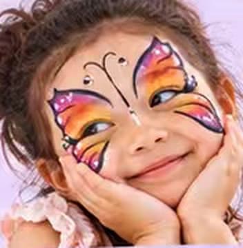 A smiling girl with an orange and purple butterfly face-painted around her eyes